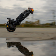 Person on a unicycle performing a trick in an open area with a cloudy sky.