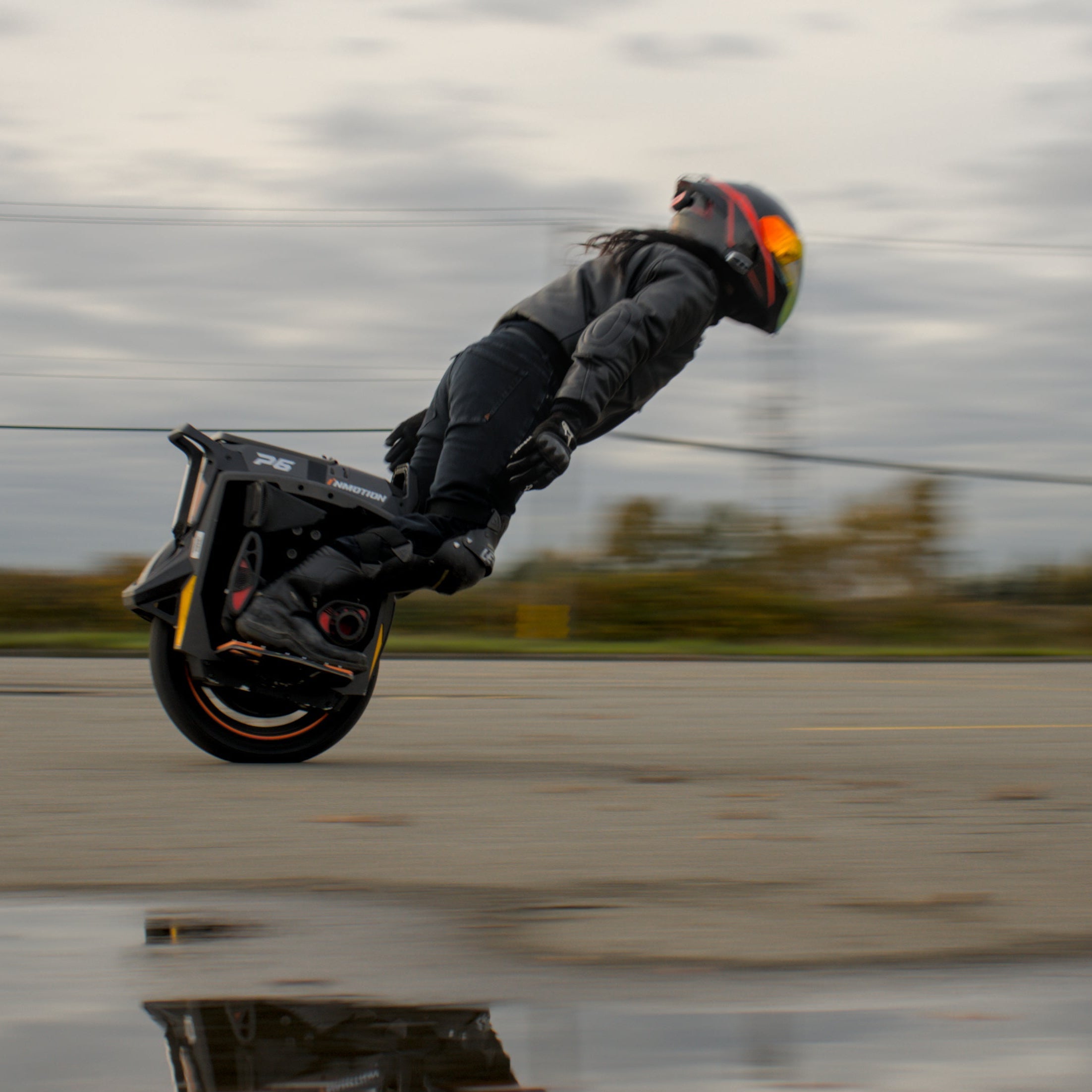 Person on a unicycle performing a trick in an open area with a cloudy sky.