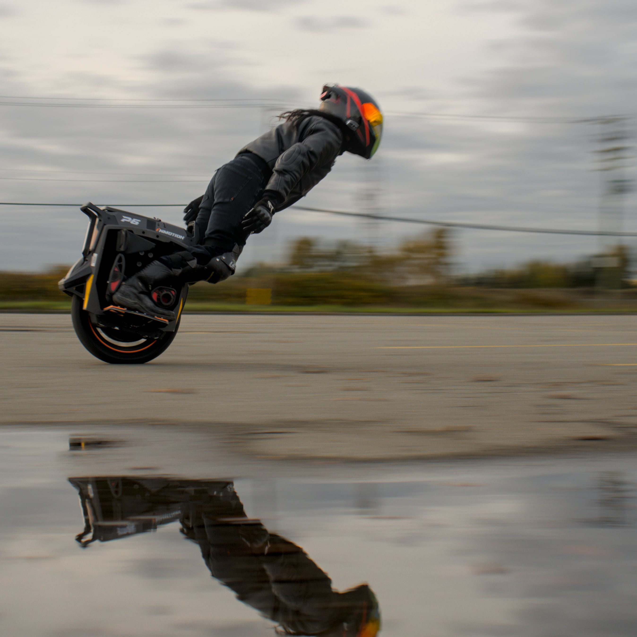 Person on a unicycle performing a trick in an open area with a cloudy sky.