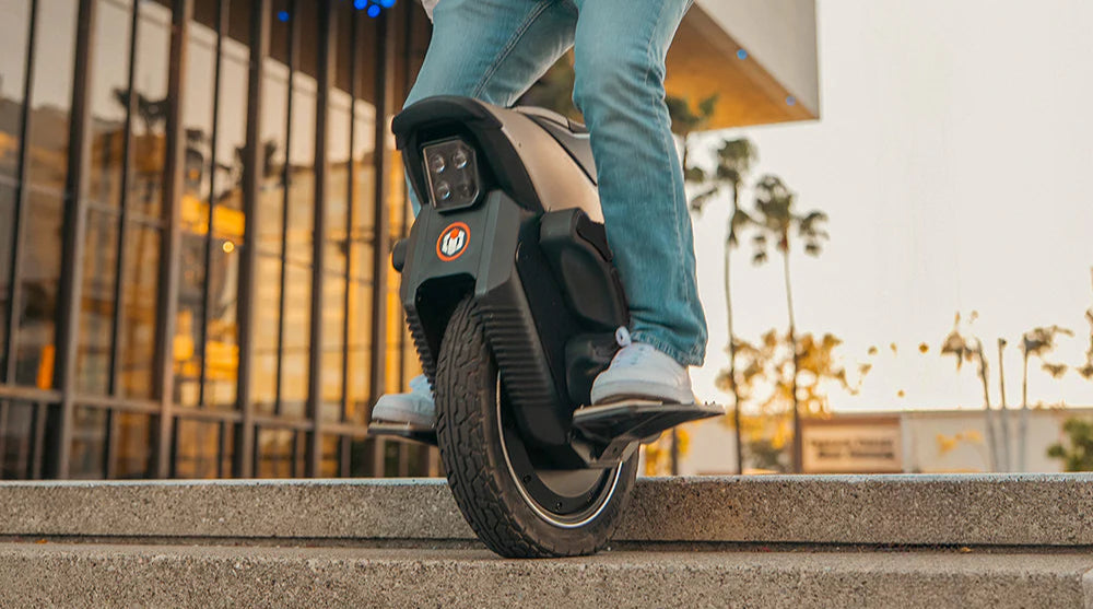 Person riding a unicycle on steps with a building and palm trees in the background