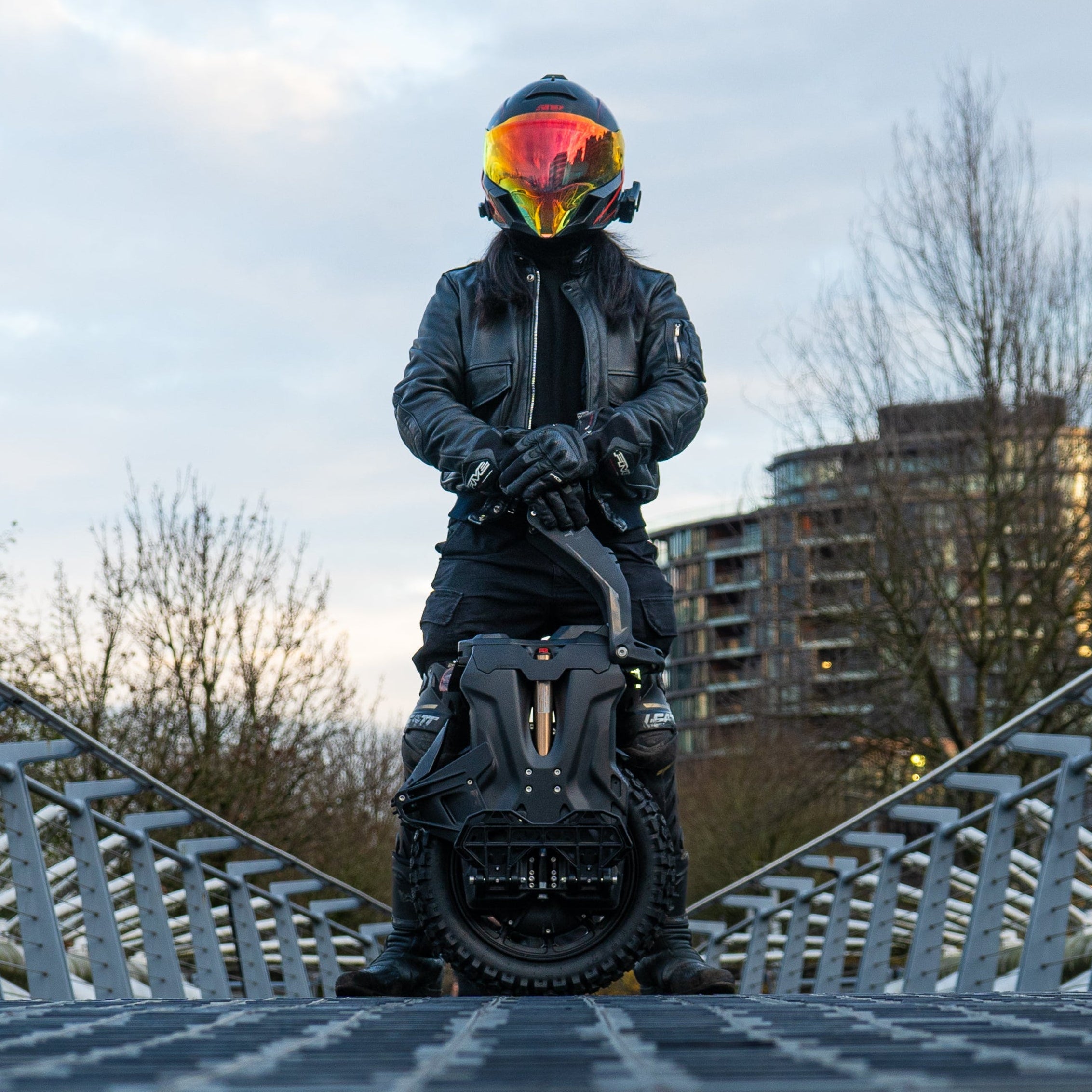 Person riding a scooter on a bridge with a cityscape in the background