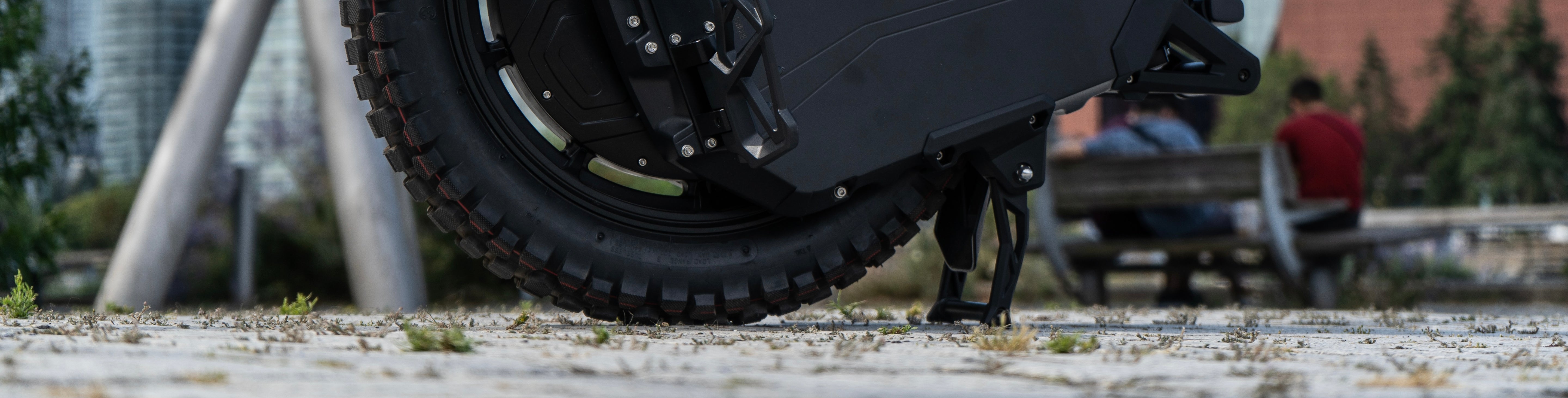 Close-up of a black tire on a vehicle with people and a bench in the background